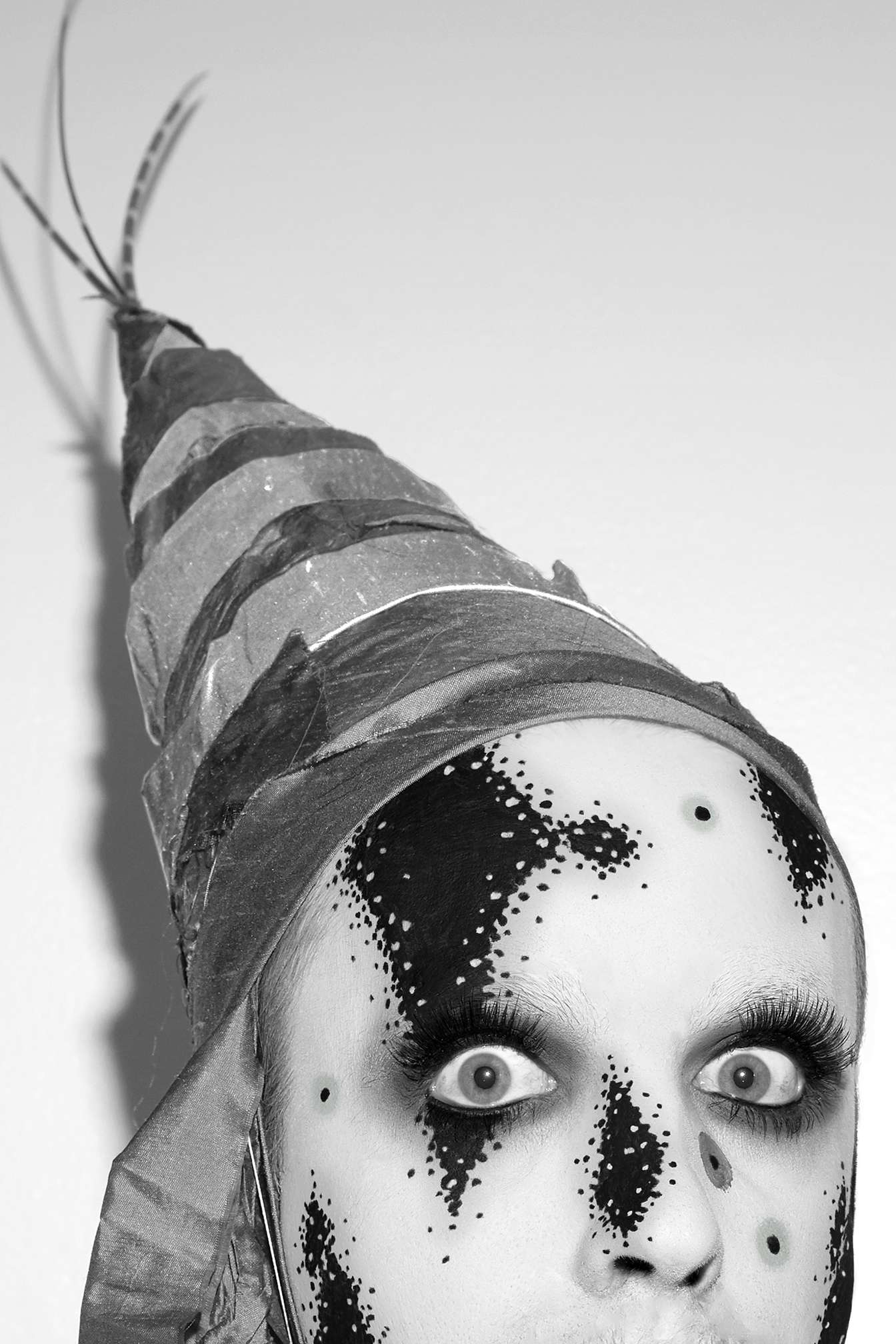 Detail of Jesse with graphic black and white facepaint on and a fabric cone on his head against a white background